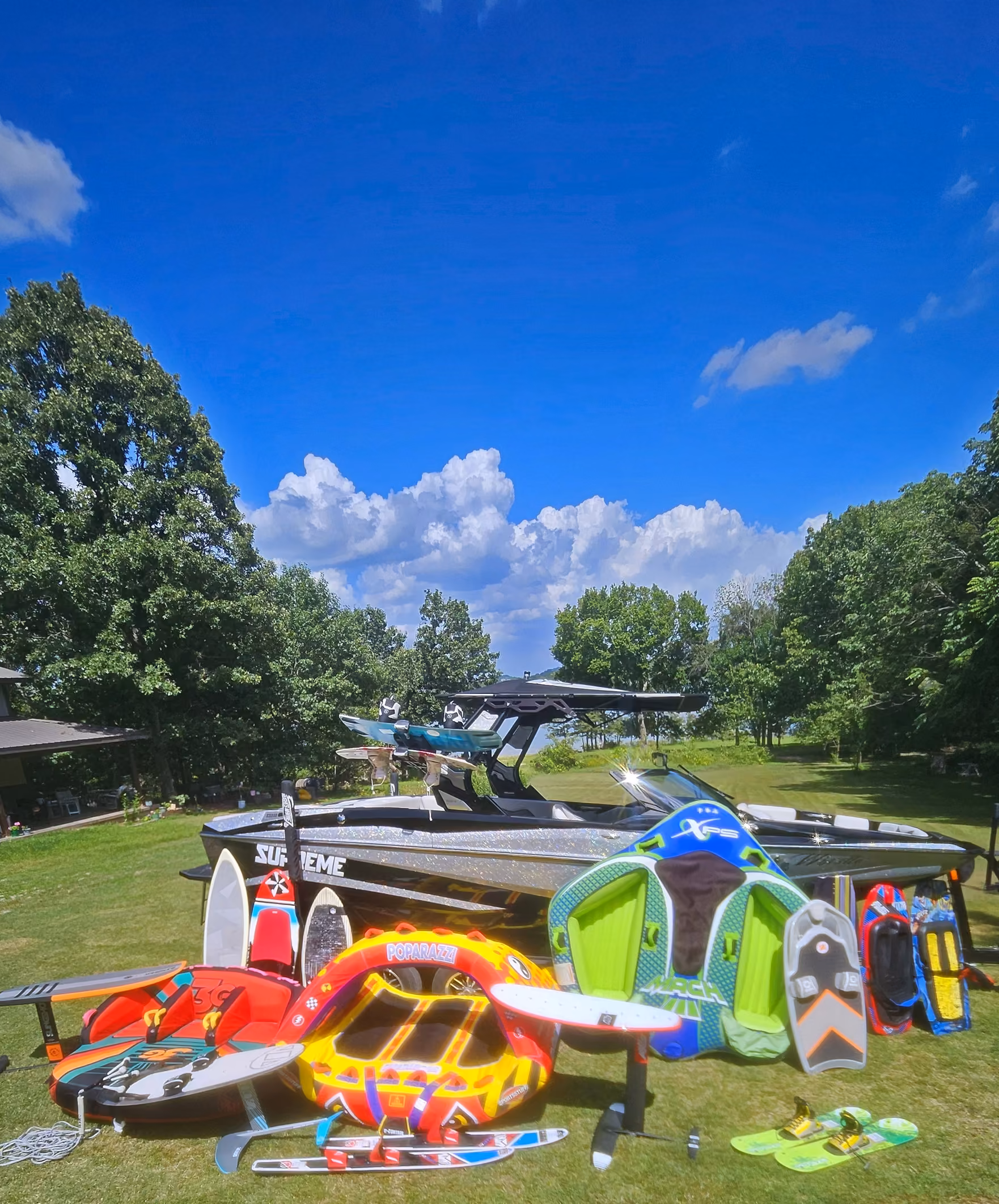 The Supreme ZS232 on the lawn with the gear laid out in front of it: tubes, surfboards, a foil board, wakeboards and water skis.